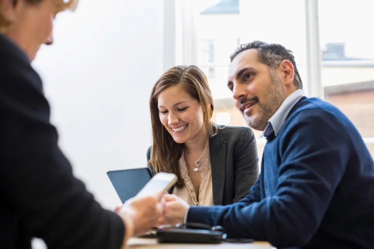 Two colleagues smiling while reviewing something on a tablet in an office meeting