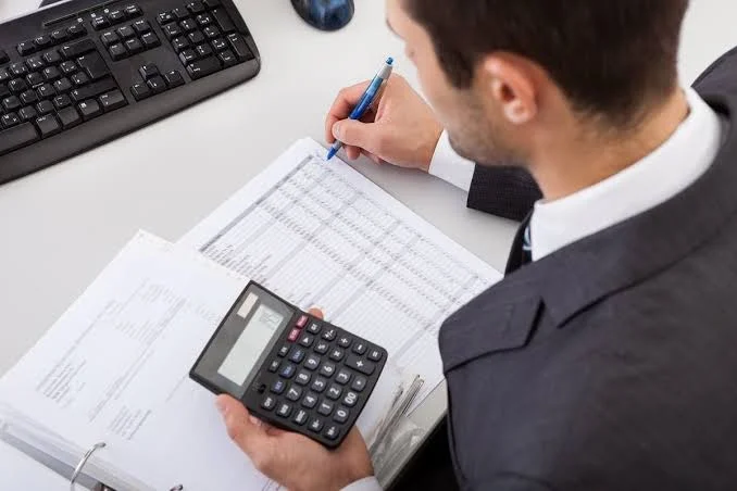 A bookkeeper using a calculator while reviewing figures in a ledger