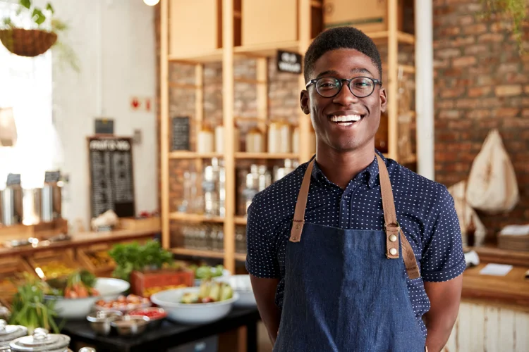 A smiling shop owner in an apron standing in his store