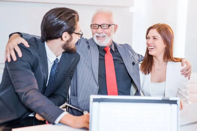 Three colleagues laughing together with their arms around each other's shoulders